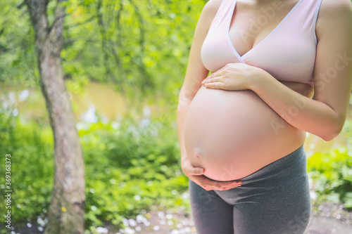 Beautiful young pregnant woman doing yoga exercising in park outdoor. Sitting and relaxing on pink yoga mat. Active future mother sport lifestyle. Healthy pregnancy concept