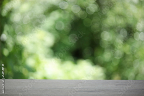 Empty wooden table top planks with beautiful nature blurred green leaf background under sunlight