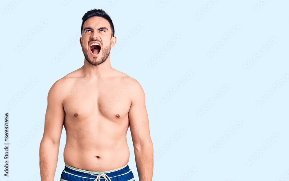 Young handsome man wearing swimwear angry and mad screaming frustrated and furious, shouting with anger. rage and aggressive concept. Young handsome man wearing swimwear angry and mad screaming frustrated and furious, shouting with anger. rage and aggressive concept.