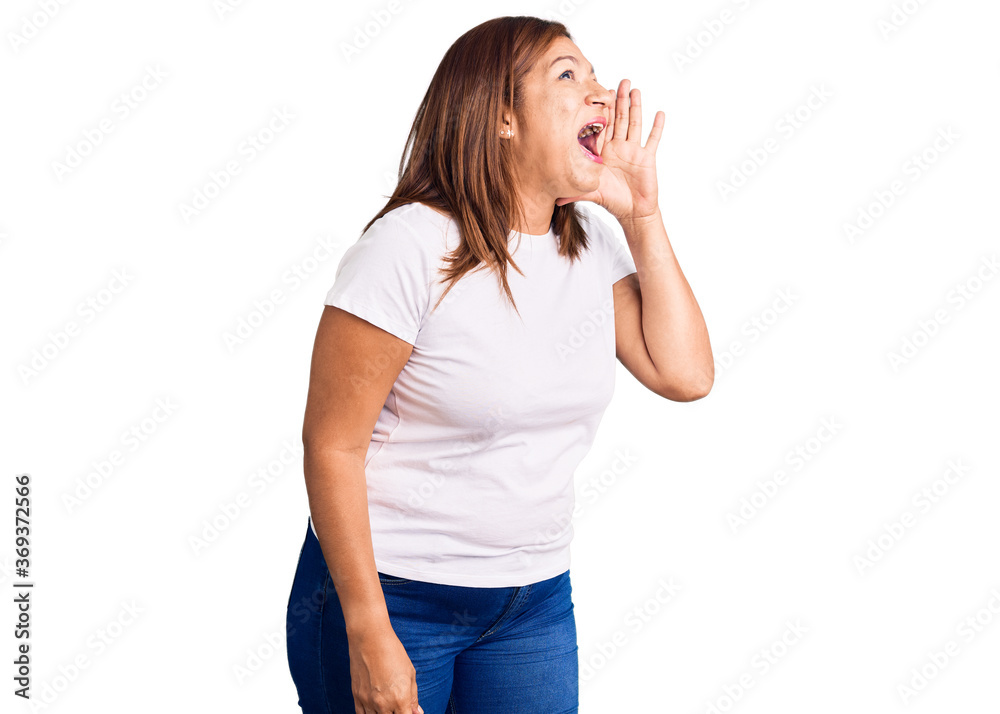 Middle age latin woman wearing casual white tshirt shouting and screaming loud to side with hand on mouth. communication concept. Middle age latin woman wearing casual white tshirt shouting and screaming loud to side with hand on mouth. communication concept.
