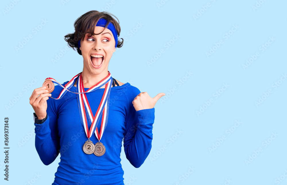 Beautiful young woman with short hair wearing winner medals pointing thumb up to the side smiling happy with open mouth Beautiful young woman with short hair wearing winner medals pointing thumb up to the side smiling happy with open mouth