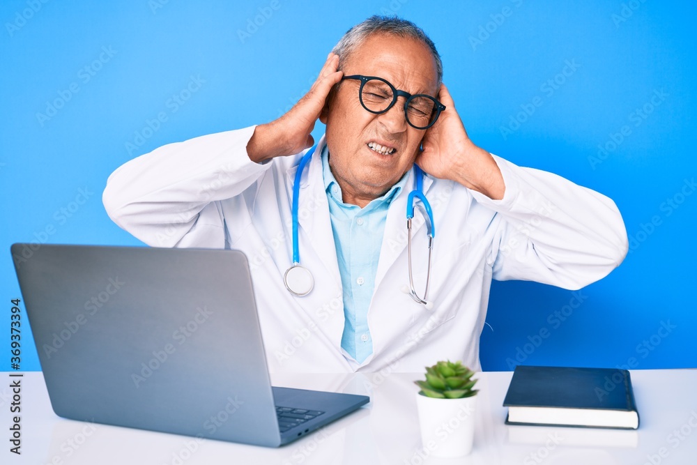Senior handsome man with gray hair wearing doctor uniform working using computer laptop covering ears with fingers with annoyed expression for the noise of loud music. deaf concept. Senior handsome man with gray hair wearing doctor uniform working using computer laptop covering ears with fingers with annoyed expression for the noise of loud music. deaf concept.