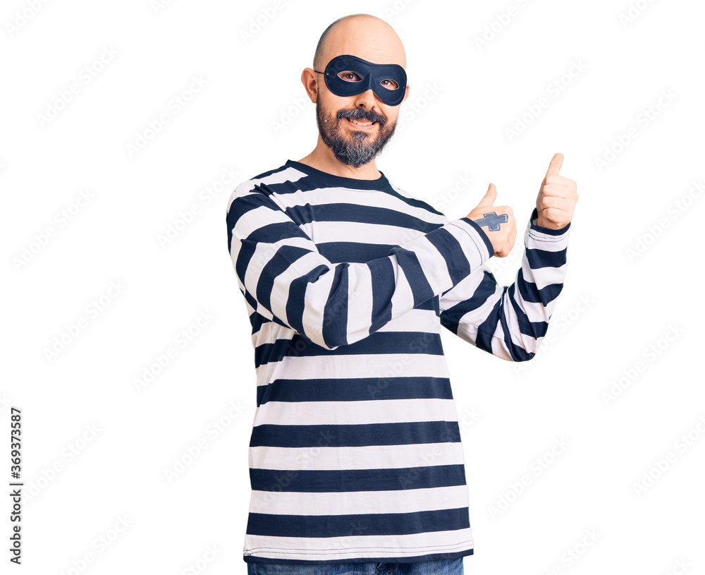 Naklejka premium Young handsome man wearing burglar mask pointing to the back behind with hand and thumbs up, smiling confident