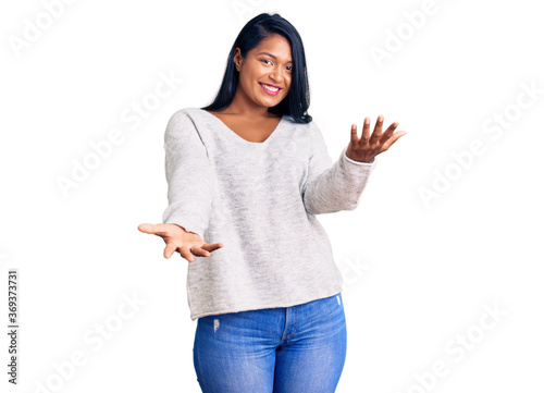 Hispanic woman with long hair wearing casual clothes smiling cheerful with open arms as friendly welcome, positive and confident greetings