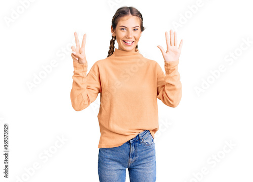 Beautiful caucasian woman with blonde hair wearing casual winter sweater showing and pointing up with fingers number seven while smiling confident and happy.