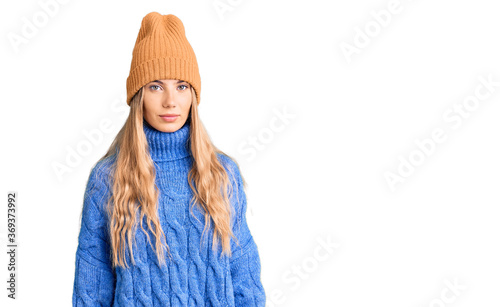 Beautiful caucasian woman with blonde hair wearing wool sweater and winter hat with serious expression on face. simple and natural looking at the camera. photo