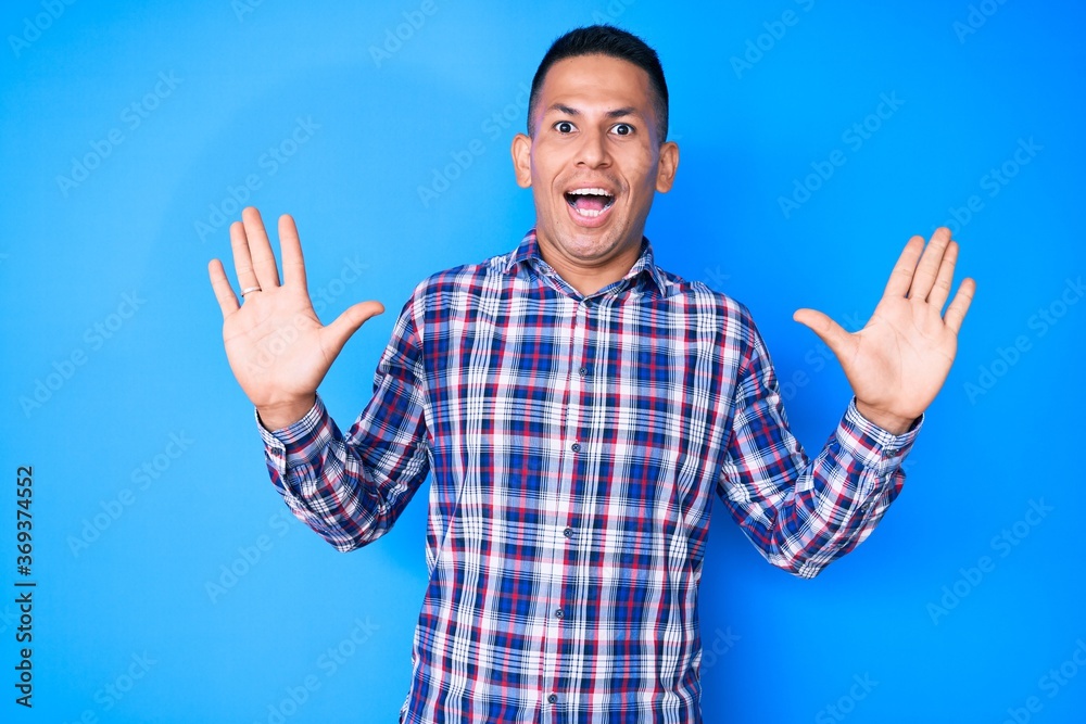 Young handsome latin man wearing casual clothes celebrating crazy and amazed for success with arms raised and open eyes screaming excited. winner concept Young handsome latin man wearing casual clothes celebrating crazy and amazed for success with arms raised and open eyes screaming excited. winner concept