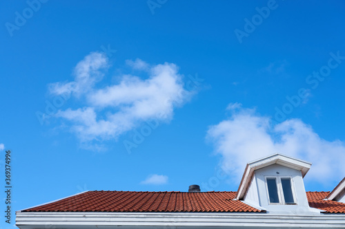 A roof of a house with a clear blue sky and white clouds on a background. Copy space.