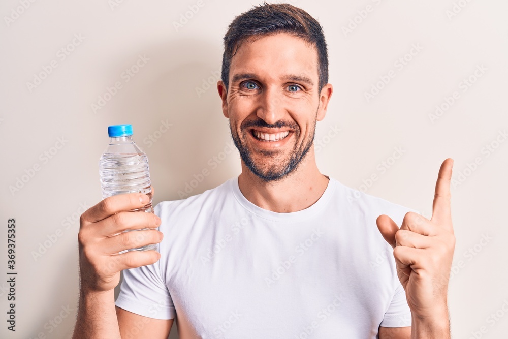 Young handsome man drinking bottle of water to refreshment over isolated white background smiling happy pointing with hand and finger to the side Young handsome man drinking bottle of water to refreshment over isolated white background smiling happy pointing with hand and finger to the side