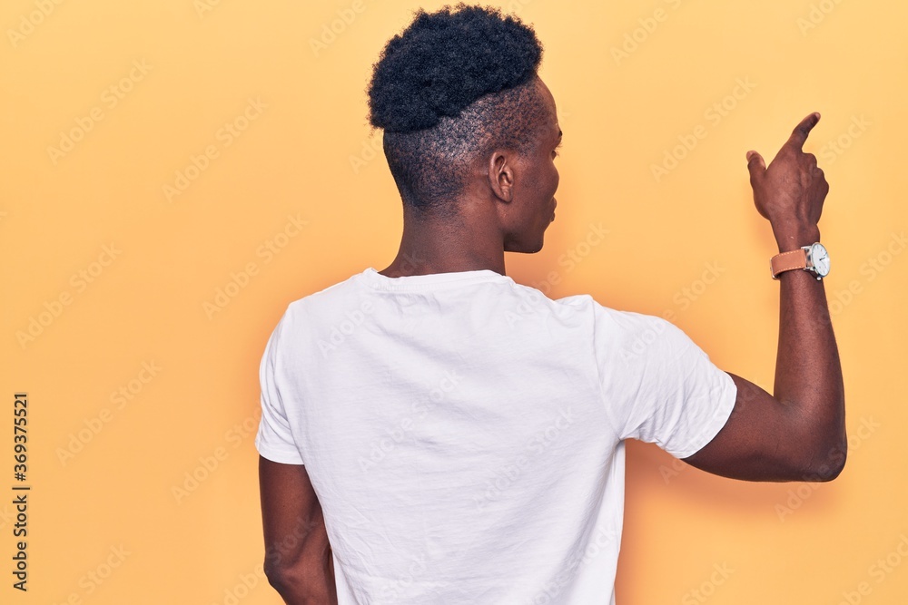 Young african american man wearing casual clothes posing backwards pointing ahead with finger hand Young african american man wearing casual clothes posing backwards pointing ahead with finger hand