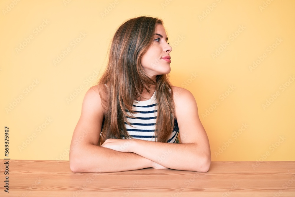 Beautiful young caucasian woman wearing casual clothes sitting on the table looking to side, relax profile pose with natural face with confident smile. Beautiful young caucasian woman wearing casual clothes sitting on the table looking to side, relax profile pose with natural face with confident smile.