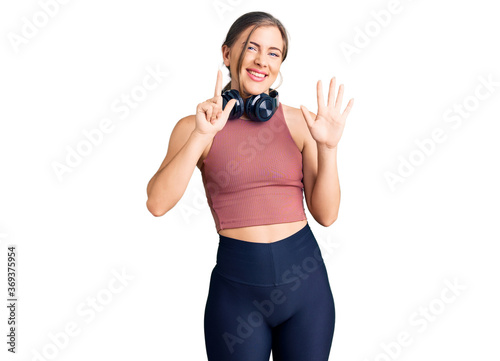 Beautiful caucasian young woman wearing gym clothes and using headphones showing and pointing up with fingers number seven while smiling confident and happy. © Krakenimages.com