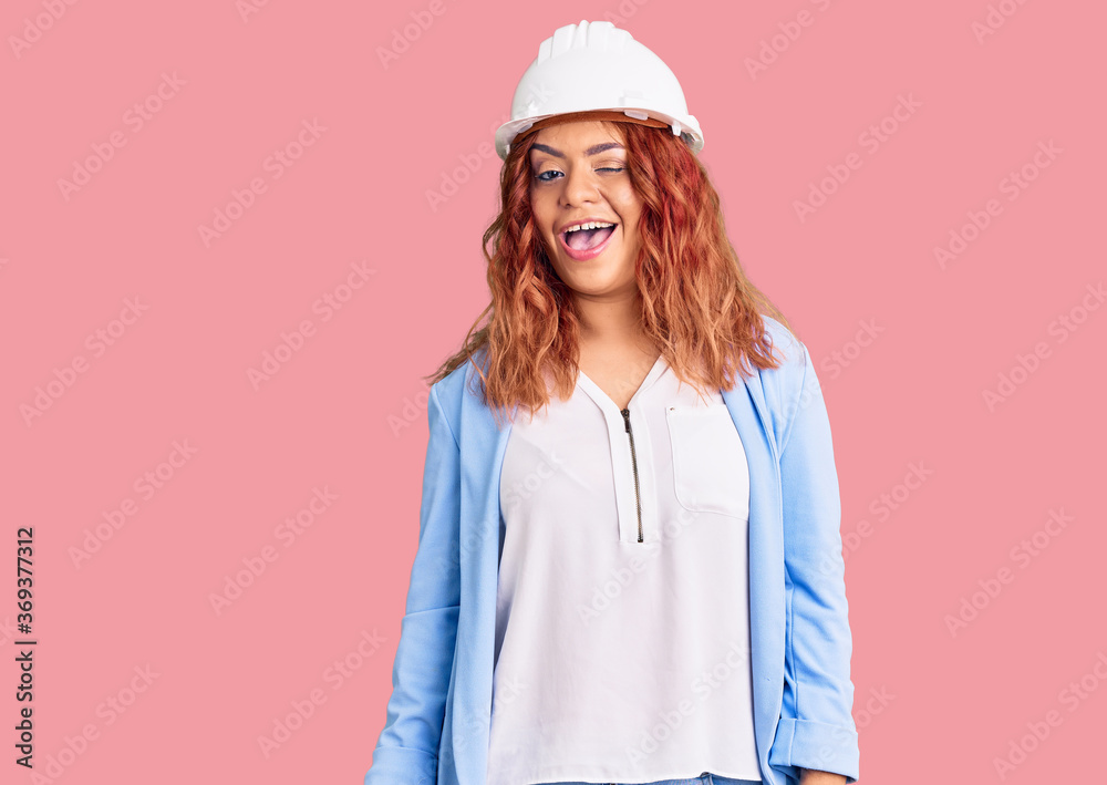 Young latin woman wearing architect hardhat winking looking at the camera with sexy expression, cheerful and happy face. Young latin woman wearing architect hardhat winking looking at the camera with sexy expression, cheerful and happy face.