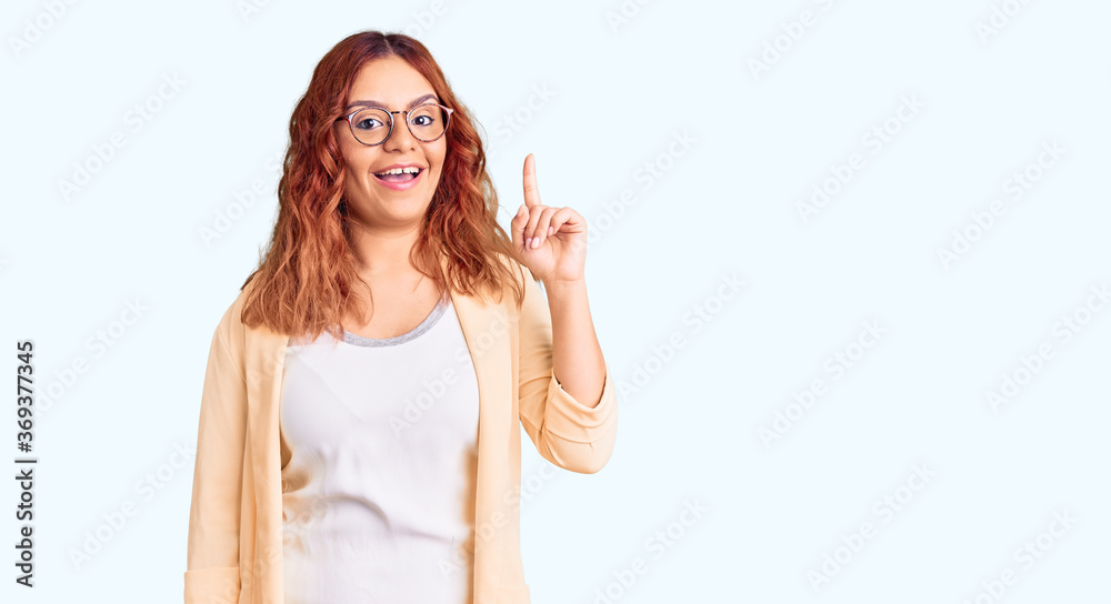 Young latin woman wearing business clothes showing and pointing up with finger number one while smiling confident and happy.