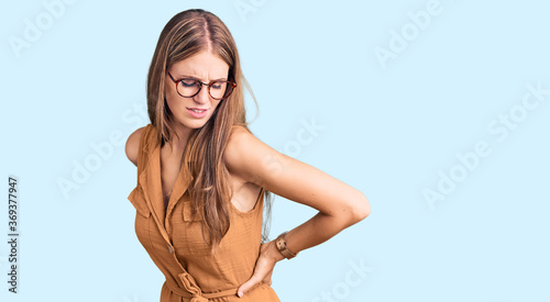 Young beautiful blonde woman wearing casual clothes and glasses suffering of backache, touching back with hand, muscular pain