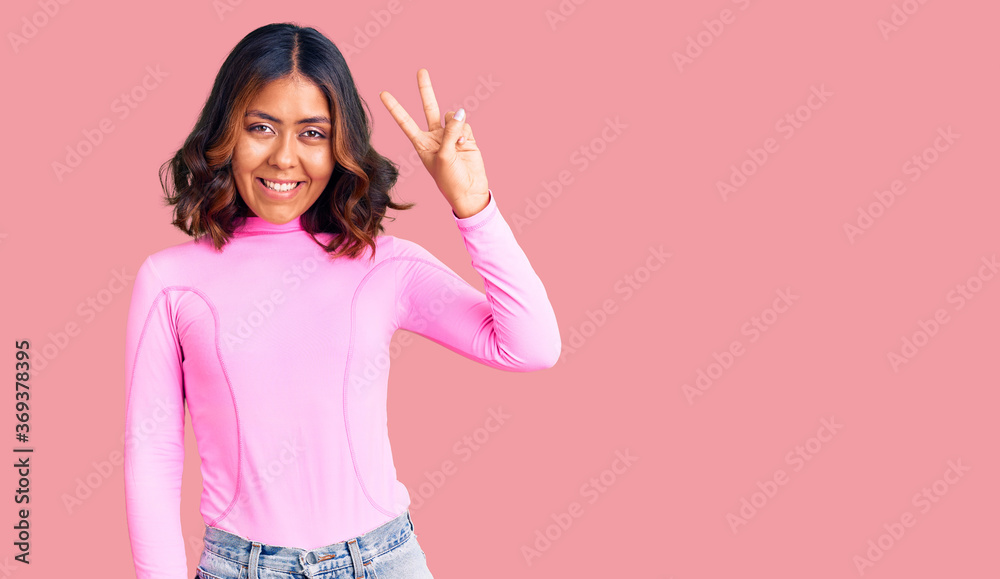 Young beautiful mixed race woman wearing pink shirt smiling with happy face winking at the camera doing victory sign. number two. Young beautiful mixed race woman wearing pink shirt smiling with happy face winking at the camera doing victory sign. number two.