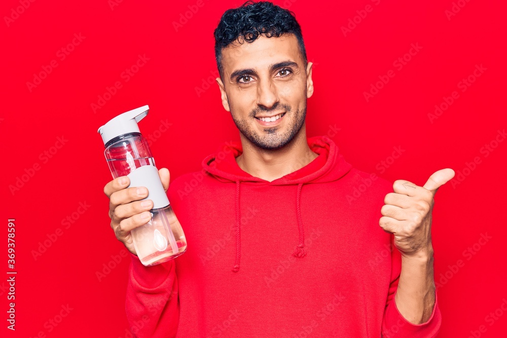 Young hispanic man drinking bottle of water smiling happy and positive, thumb up doing excellent and approval sign Young hispanic man drinking bottle of water smiling happy and positive, thumb up doing excellent and approval sign