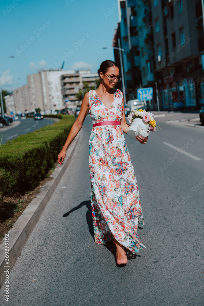 Young beautiful stylish caucasian woman model in summer dress with flower box in her hand on the street Young beautiful stylish caucasian woman model in summer dress with flower box in her hand on the street