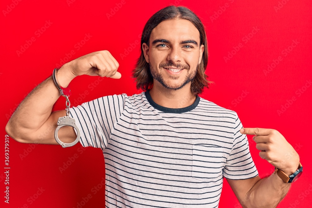 Fototapeta premium Young handsome man wearing prisoner handcuffs pointing finger to one self smiling happy and proud