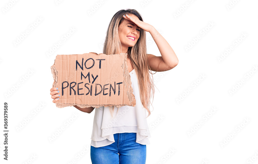 Young beautiful blonde woman holding not my president cardboard banner stressed and frustrated with hand on head, surprised and angry face Young beautiful blonde woman holding not my president cardboard banner stressed and frustrated with hand on head, surprised and angry face