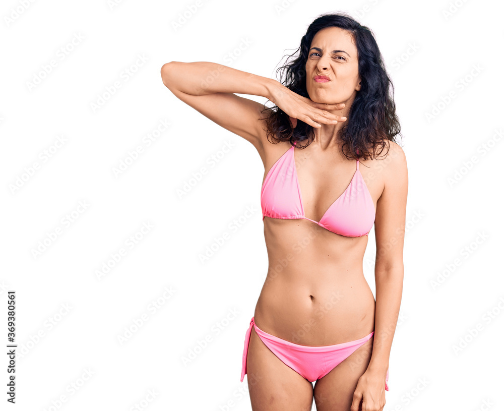 Young beautiful hispanic woman wearing bikini cutting throat with hand as knife, threaten aggression with furious violence Young beautiful hispanic woman wearing bikini cutting throat with hand as knife, threaten aggression with furious violence