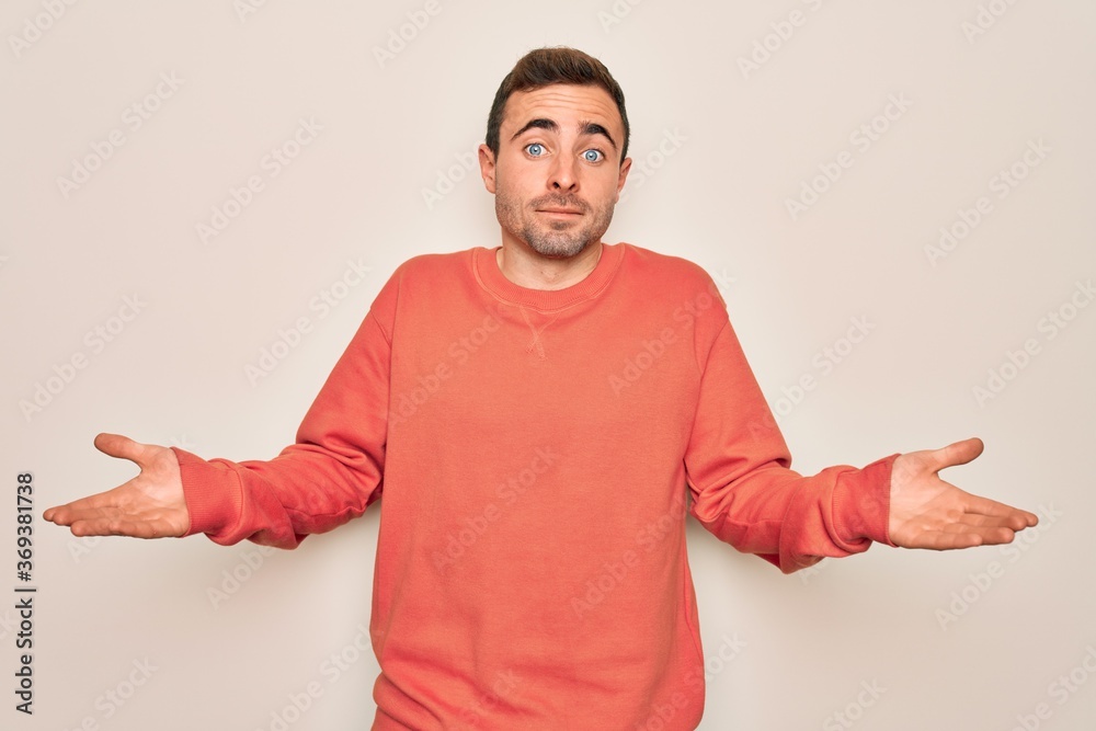 Young handsome man with blue eyes wearing casual sweater standing over white background clueless and confused expression with arms and hands raised. Doubt concept. Young handsome man with blue eyes wearing casual sweater standing over white background clueless and confused expression with arms and hands raised. Doubt concept.