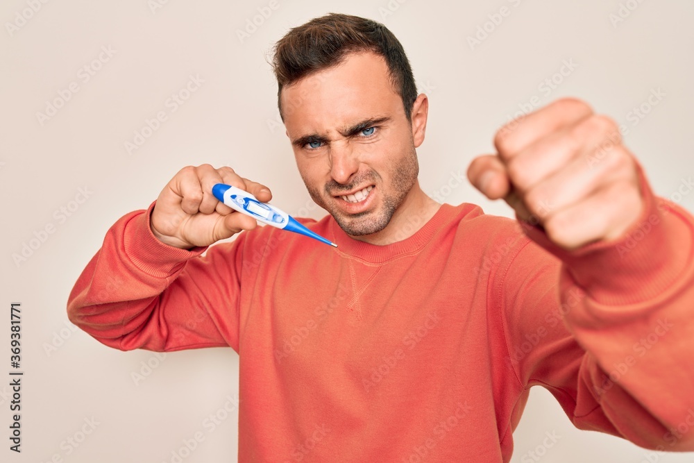 Young handsome man with blue eyes measuring temperature using digital thermometer annoyed and frustrated shouting with anger, yelling crazy with anger and hand raised Young handsome man with blue eyes measuring temperature using digital thermometer annoyed and frustrated shouting with anger, yelling crazy with anger and hand raised