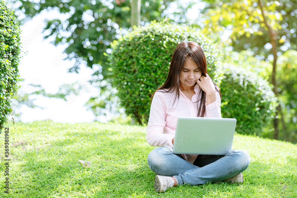 Asian woman sitting green park using laptop computer. Woman working on laptop happy entrepreneur business using notebook with hands typing on keyboard home office during coronavirus quarantine period Asian woman sitting green park using laptop computer. Woman working on laptop happy entrepreneur business using notebook with hands typing on keyboard home office during coronavirus quarantine period