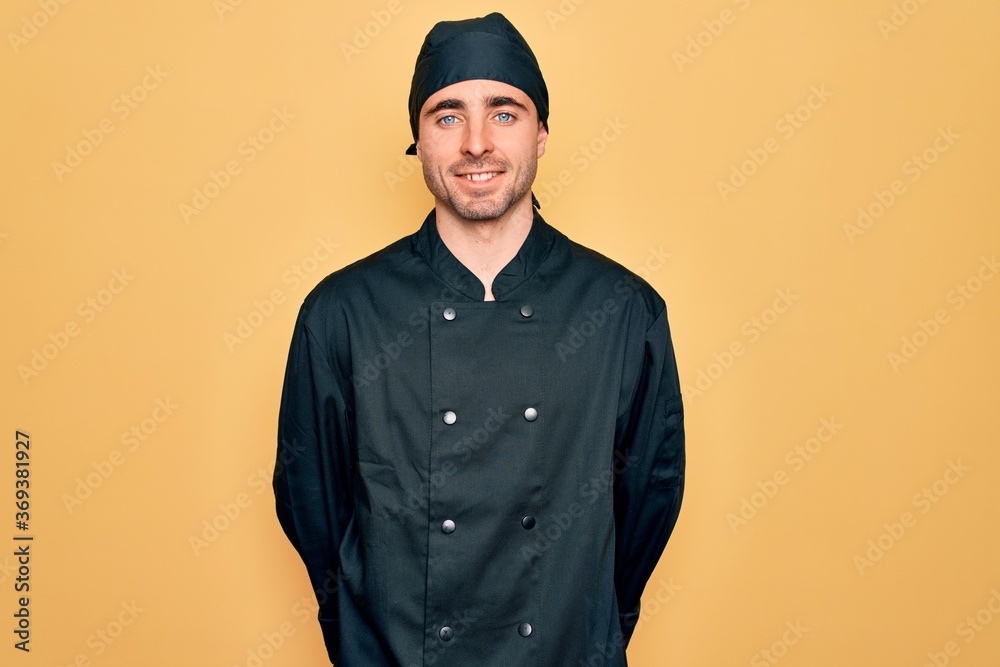 Young handsome cooker man with blue eyes wearing uniform and hat over yellow background with a happy and cool smile on face. Lucky person. Young handsome cooker man with blue eyes wearing uniform and hat over yellow background with a happy and cool smile on face. Lucky person.