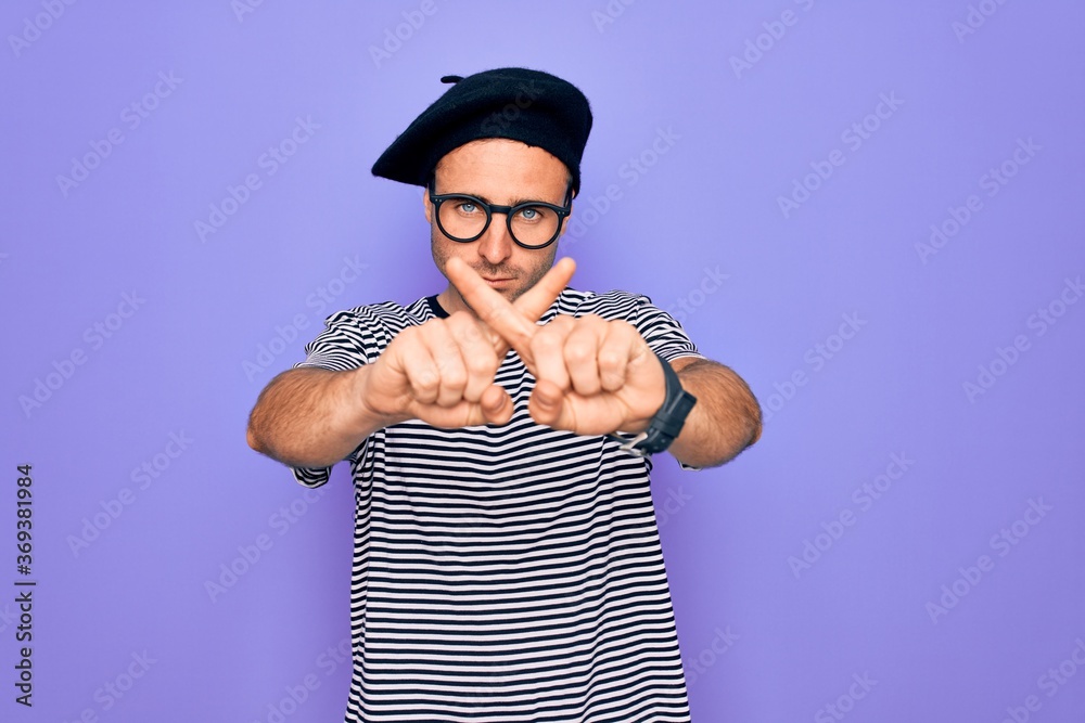 Handsome man with blue eyes wearing striped t-shirt and french beret over purple background Rejection expression crossing fingers doing negative sign Handsome man with blue eyes wearing striped t-shirt and french beret over purple background Rejection expression crossing fingers doing negative sign