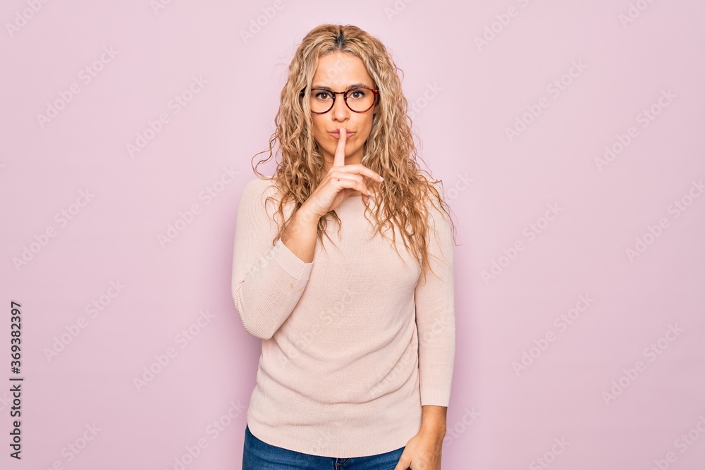 Young beautiful blonde woman wearing casual sweater and glasses over pink background asking to be quiet with finger on lips. Silence and secret concept. Young beautiful blonde woman wearing casual sweater and glasses over pink background asking to be quiet with finger on lips. Silence and secret concept.