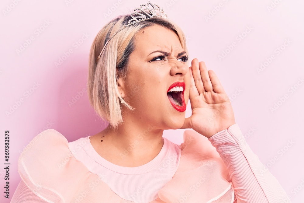 Beautiful blonde plus size woman wearing pincess tiara with diamonds over pink background shouting and screaming loud to side with hand on mouth. Communication concept. Beautiful blonde plus size woman wearing pincess tiara with diamonds over pink background shouting and screaming loud to side with hand on mouth. Communication concept.