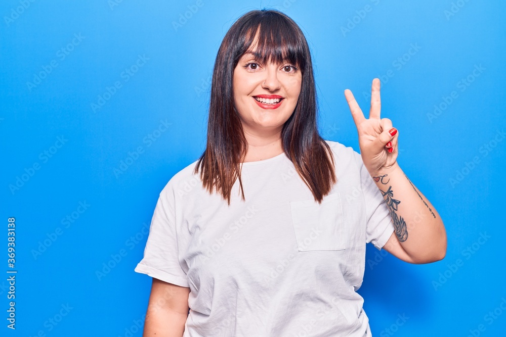 Young plus size woman wearing casual clothes smiling with happy face winking at the camera doing victory sign. number two. Young plus size woman wearing casual clothes smiling with happy face winking at the camera doing victory sign. number two.