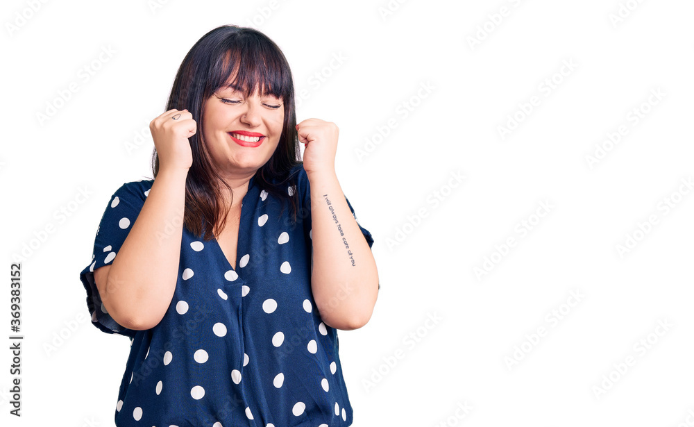 Young plus size woman wearing casual clothes excited for success with arms raised and eyes closed celebrating victory smiling. winner concept. Young plus size woman wearing casual clothes excited for success with arms raised and eyes closed celebrating victory smiling. winner concept.