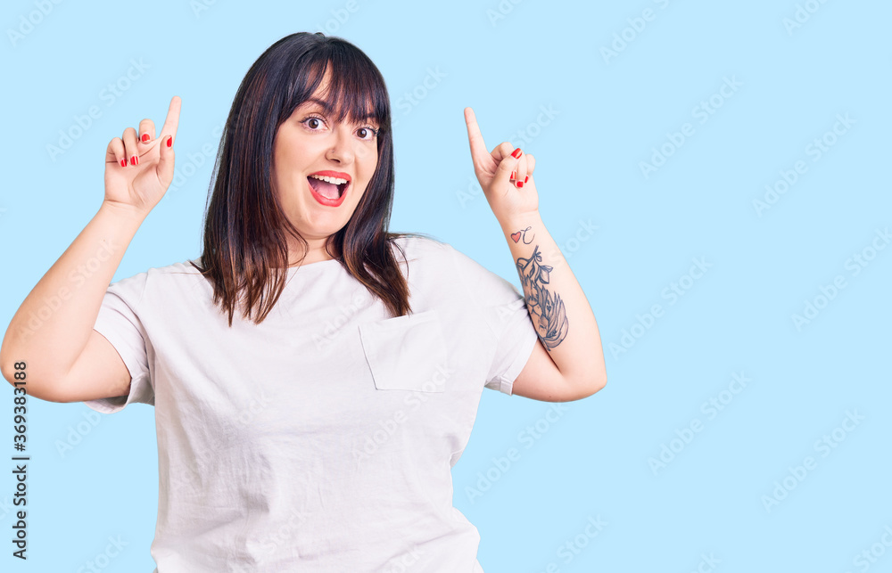 Young plus size woman wearing casual clothes smiling amazed and surprised and pointing up with fingers and raised arms. Young plus size woman wearing casual clothes smiling amazed and surprised and pointing up with fingers and raised arms.