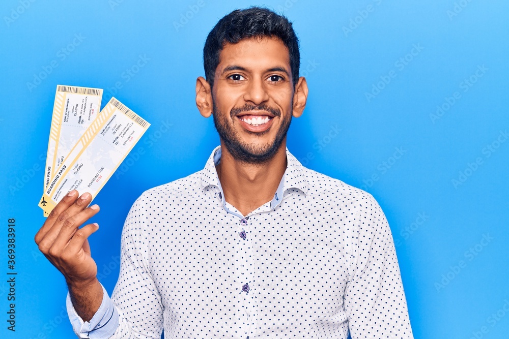 Young latin man holding boarding pass looking positive and happy standing and smiling with a confident smile showing teeth Young latin man holding boarding pass looking positive and happy standing and smiling with a confident smile showing teeth