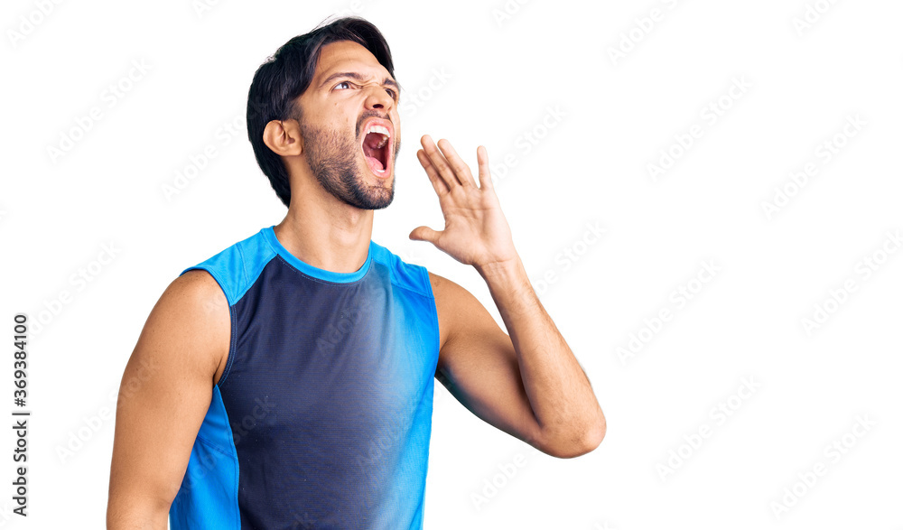 Handsome hispanic man wearing sportswear shouting and screaming loud to side with hand on mouth. communication concept. Handsome hispanic man wearing sportswear shouting and screaming loud to side with hand on mouth. communication concept.