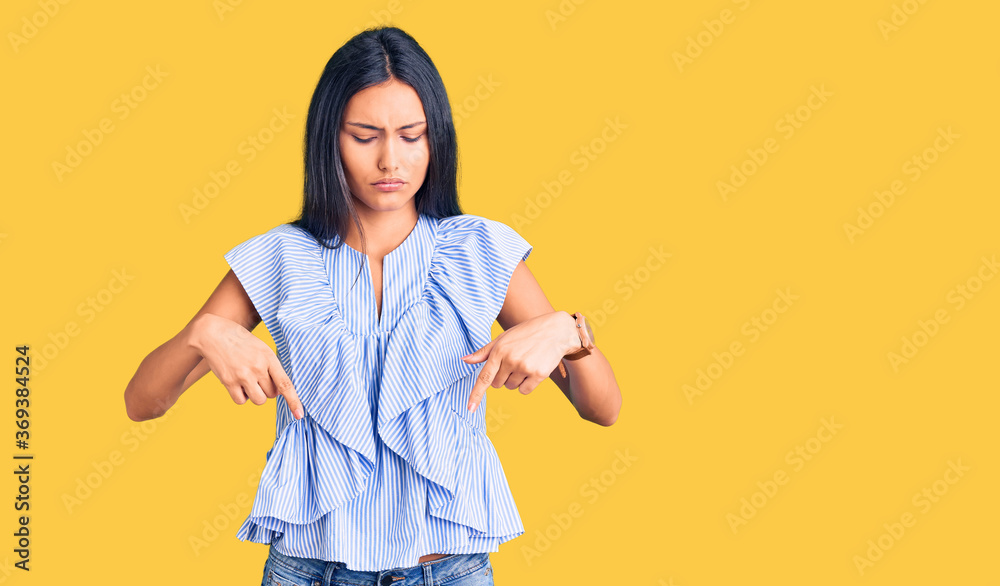 Young beautiful latin girl wearing casual clothes pointing down looking sad and upset, indicating direction with fingers, unhappy and depressed. Young beautiful latin girl wearing casual clothes pointing down looking sad and upset, indicating direction with fingers, unhappy and depressed.