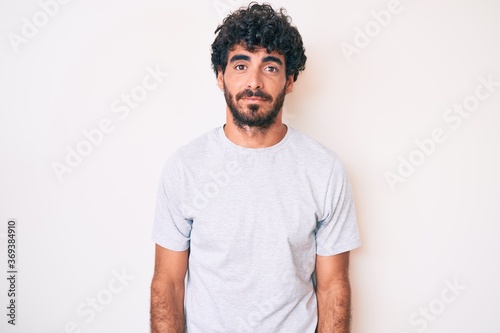 Handsome young man with curly hair and bear wearing casual tshirt with serious expression on face. simple and natural looking at the camera.