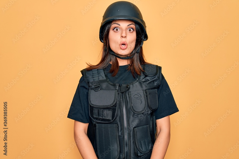 Young beautiful brunette soldier woman wearing bulletproof and security helmet afraid and shocked with surprise expression, fear and excited face.