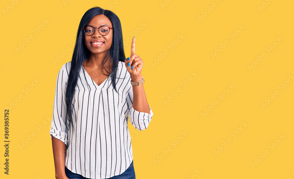 Young african american woman wearing casual clothes and glasses pointing finger up with successful idea. exited and happy. number one. Young african american woman wearing casual clothes and glasses pointing finger up with successful idea. exited and happy. number one.