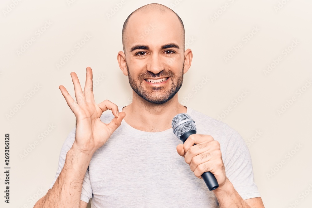 Young handsome bald man singing song using microphone doing ok sign with fingers, smiling friendly gesturing excellent symbol Young handsome bald man singing song using microphone doing ok sign with fingers, smiling friendly gesturing excellent symbol