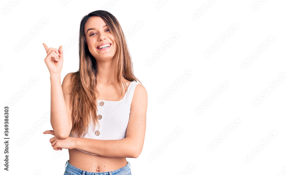 Young beautiful girl wearing casual sleeveless t shirt with a big smile on face, pointing with hand and finger to the side looking at the camera. Young beautiful girl wearing casual sleeveless t shirt with a big smile on face, pointing with hand and finger to the side looking at the camera.