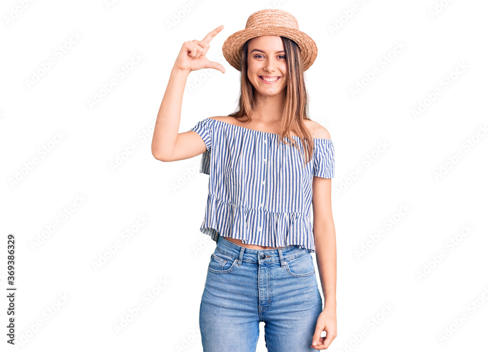Young beautiful girl wearing hat and t shirt smiling and confident gesturing with hand doing small size sign with fingers looking and the camera. measure concept. Young beautiful girl wearing hat and t shirt smiling and confident gesturing with hand doing small size sign with fingers looking and the camera. measure concept.