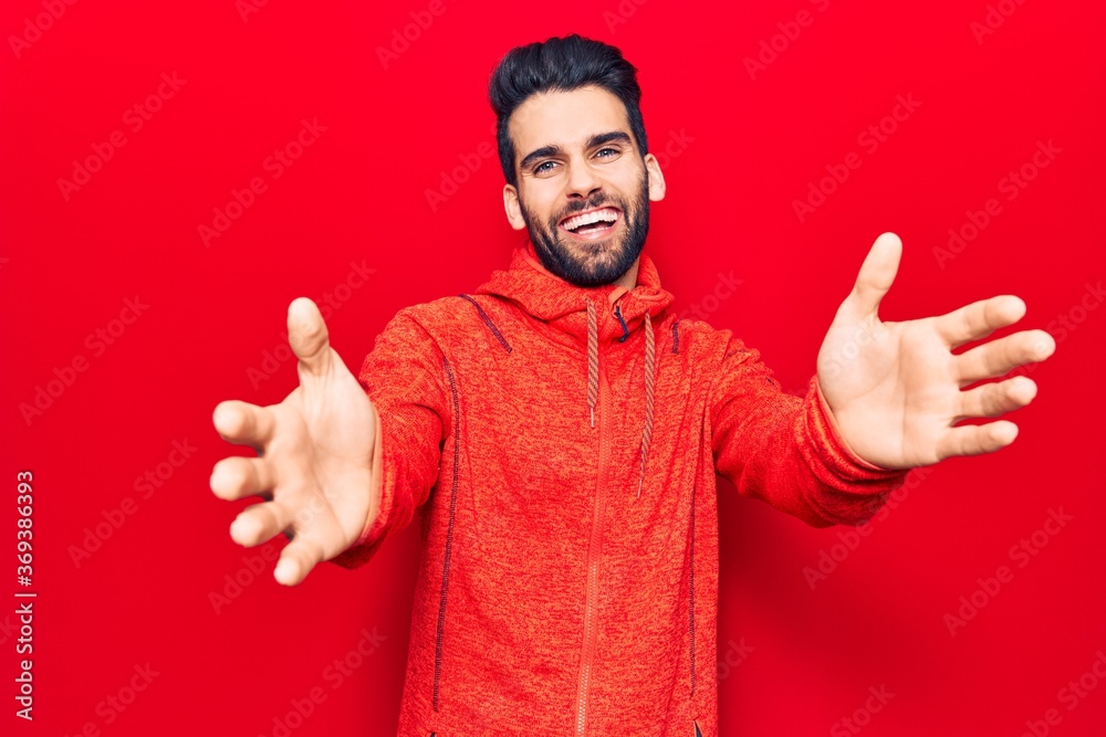 Young handsome man with beard wearing casual sweatshirt looking at the camera smiling with open arms for hug. cheerful expression embracing happiness. Young handsome man with beard wearing casual sweatshirt looking at the camera smiling with open arms for hug. cheerful expression embracing happiness.