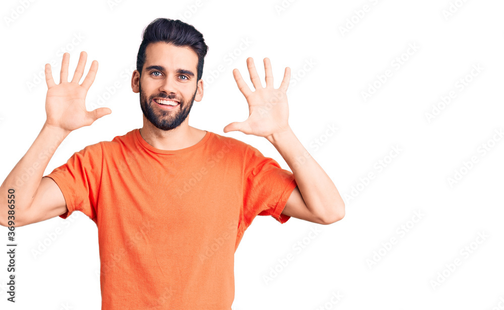 Young handsome man with beard wearing casual t-shirt showing and pointing up with fingers number ten while smiling confident and happy.