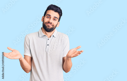 Young handsome man with beard wearing casual polo clueless and confused expression with arms and hands raised. doubt concept.