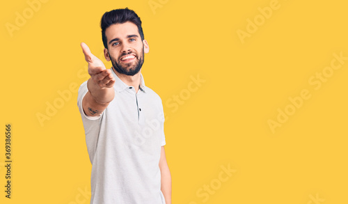Young handsome man with beard wearing casual polo smiling friendly offering handshake as greeting and welcoming. successful business.