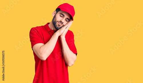 Young handsome man with beard wearing delivery uniform sleeping tired dreaming and posing with hands together while smiling with closed eyes. © Krakenimages.com