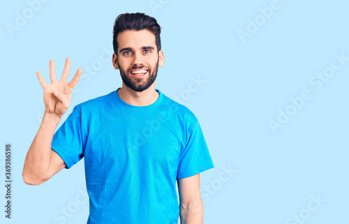 Young handsome man with beard wearing casual t-shirt showing and pointing up with fingers number four while smiling confident and happy.